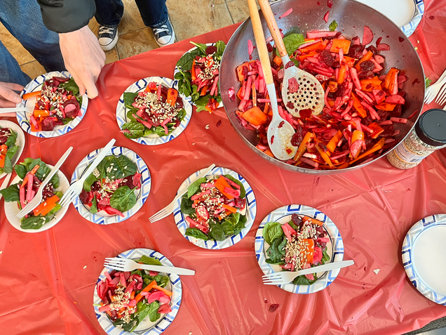 Many plates of Vegeterian Carpaccio are served next to a large bowl of the root vegetable mix. A student's hands are shown grabbing a plate.